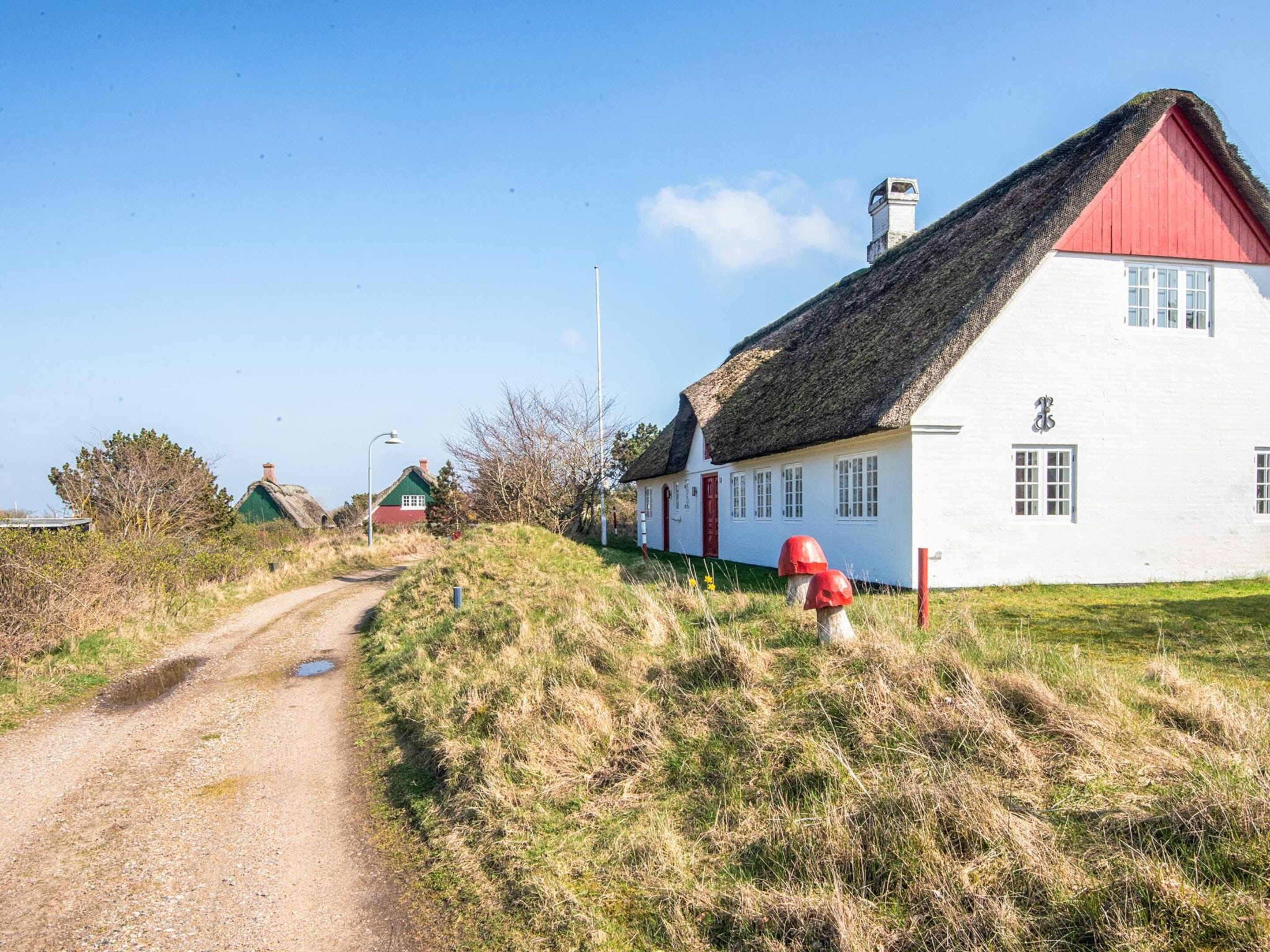 Eine ländliche Straße führt zu einer Reihe traditioneller Häuser mit Strohdächern und weißen Wänden.