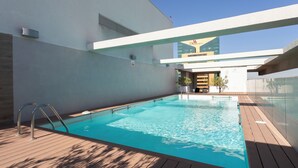 Ein Swimmingpool mit Holzterrasse, Glasbarriere und einem Gebäude im Hintergrund mit einem Schild.