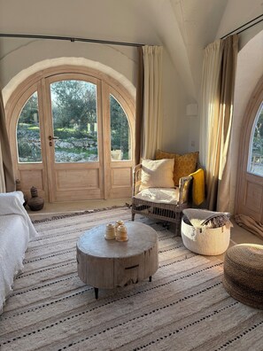 A room with a large arched window, a wicker sofa, a round wooden coffee table, and a woven pouf. - Beautiful villa with private pool and breathtaking view, enjoy in southern Italy! (Ostuni)