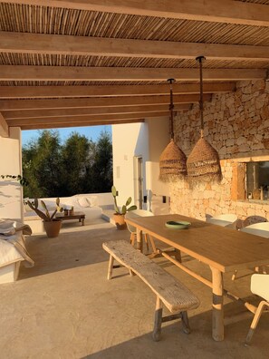 An outdoor patio with a wooden table, benches, hanging wicker lamps, and a potted cactus. - Beautiful villa with private pool and breathtaking view, enjoy in southern Italy! (Ostuni)