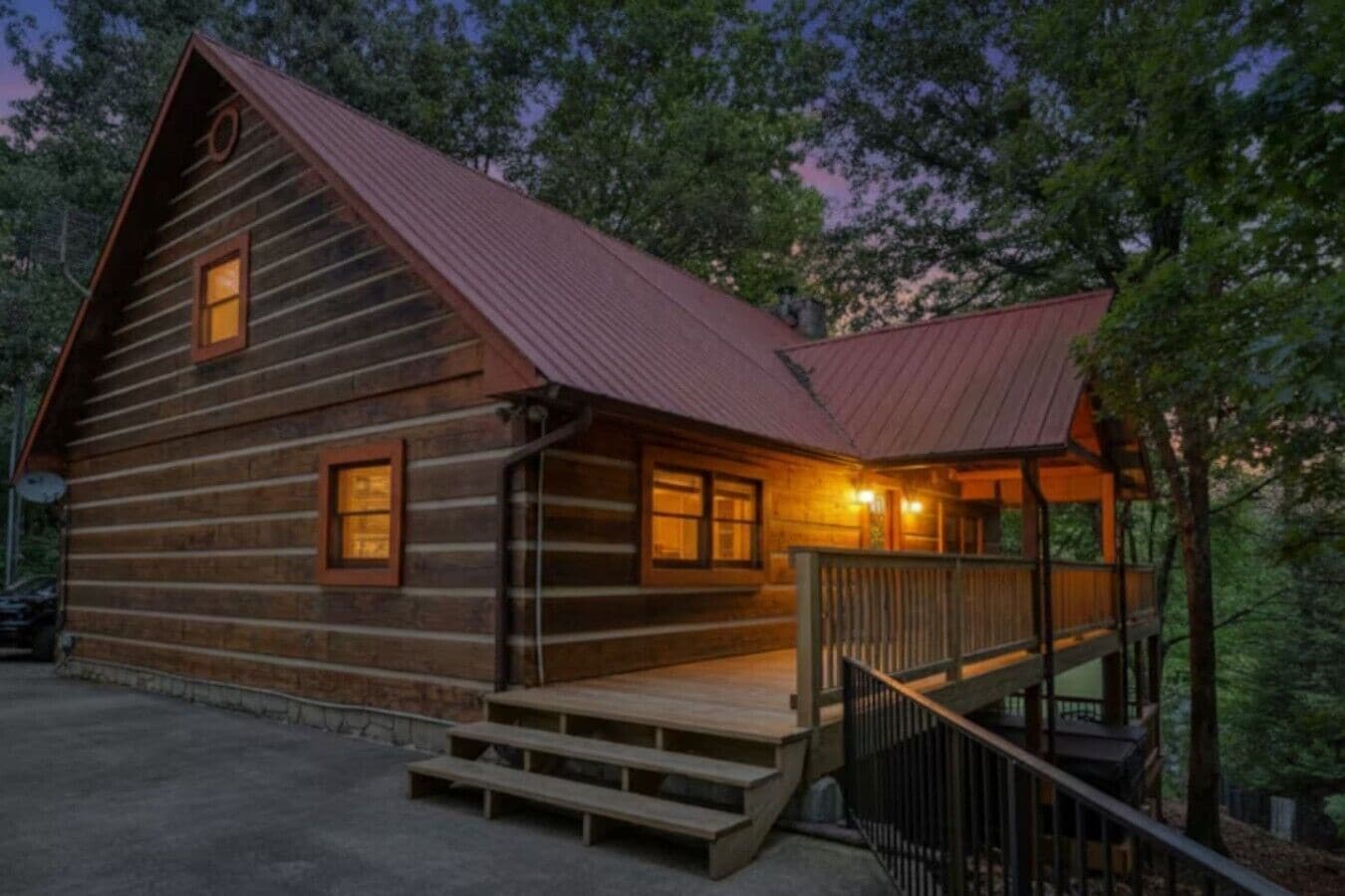 A log cabin with a metal roof, a porch with steps, and a small staircase leading to a deck.