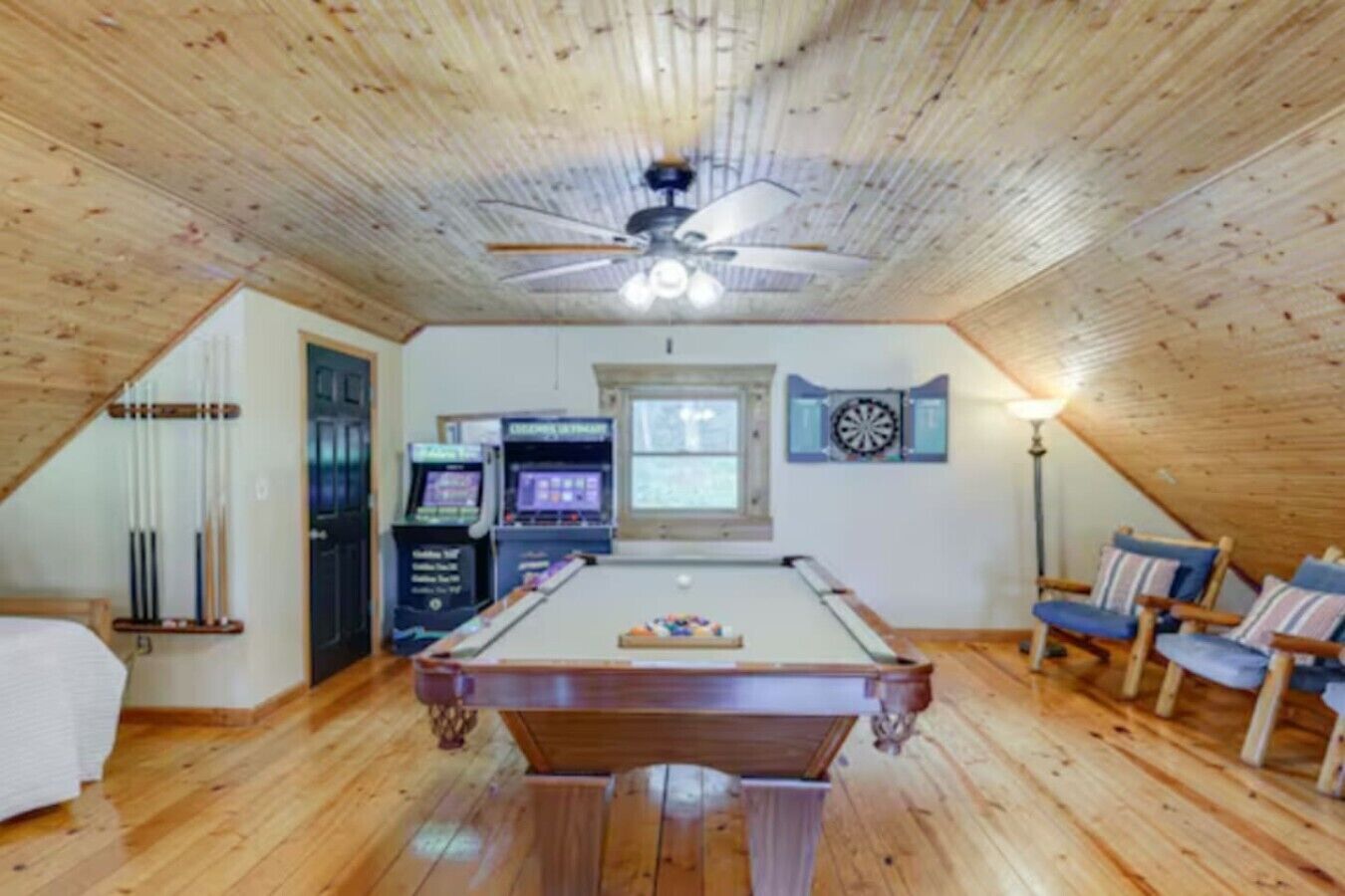 A room with a pool table, dartboard, and arcade games.
