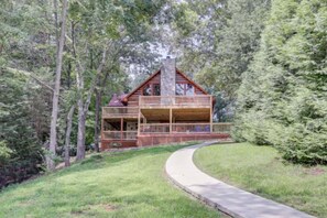 A cabin with a wrap-around porch, surrounded by dense forest.