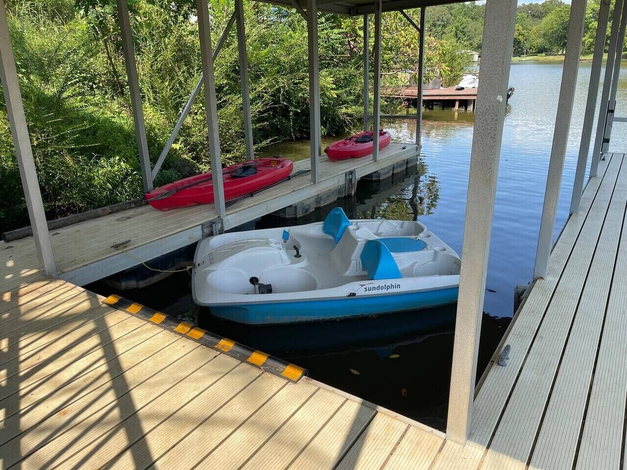 A dock with a white and blue boat named 'sundolphin' and two red kayaks.