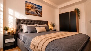Ein Schlafzimmer mit einer gepolsterten Kopfteil, einem großen Bett mit vielen Kissen, einem Nachttisch mit Lampe, einem Beistelltisch mit Büchern und einem Gemälde über dem Bett.