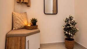 Ein Eckzimmer mit einer hölzernen Bank, einem Spiegel, einer Topfpflanze und einem Wandregal mit Hut und Pflanze.
