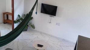 A living room with a green hammock, a sofa, a small round coffee table, and a flat-screen TV mounted on the wall. - Pousada Apart Praia Uruau (Beberibe)