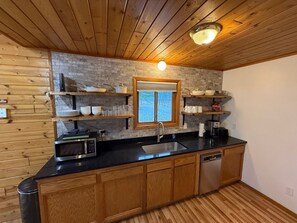 Uma cozinha com armários de madeira, bancada preta, micro-ondas embutido e janela com vista.
