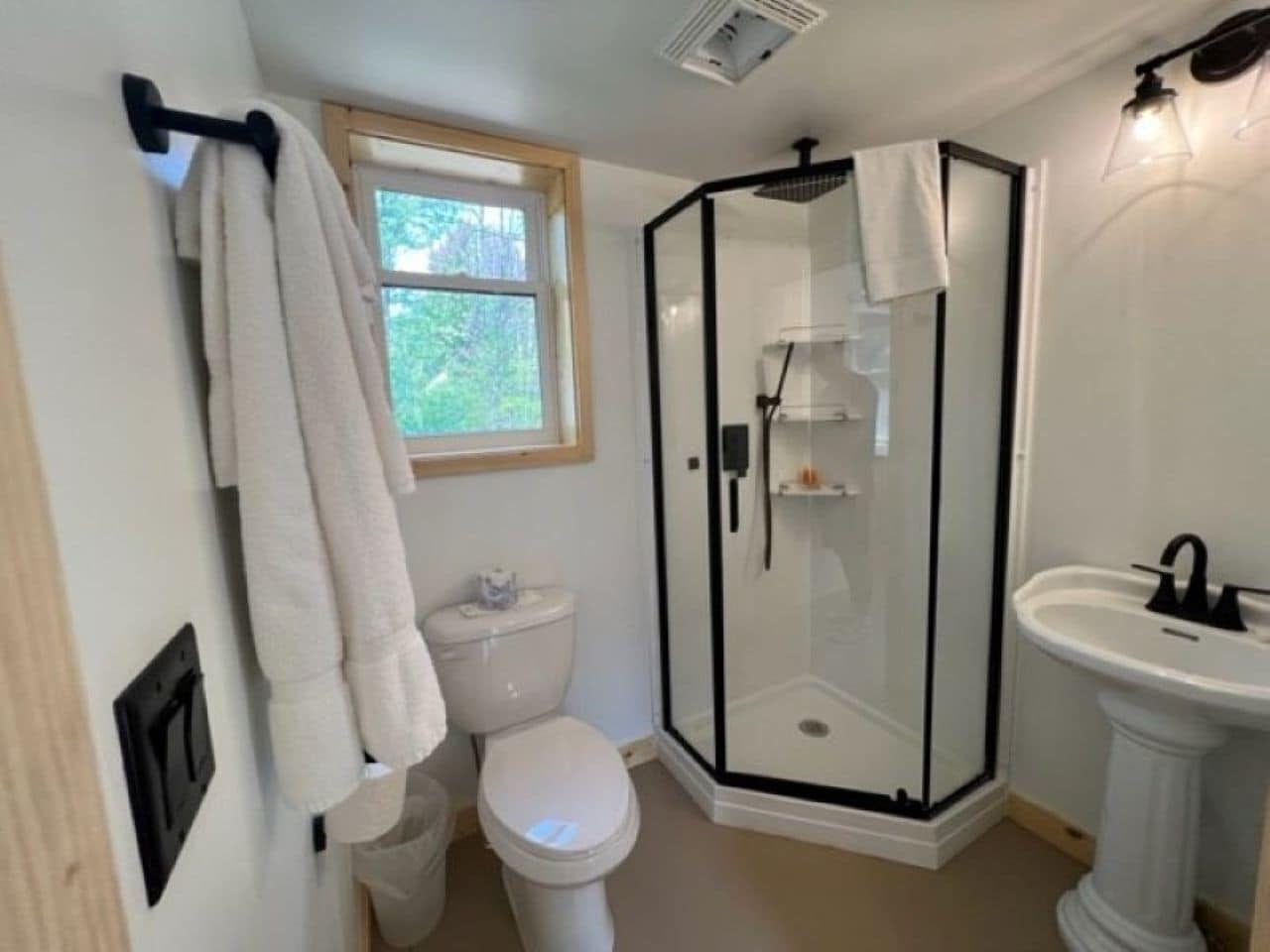 Un baño con inodoro, cabina de ducha de vidrio, lavamanos y ventana.