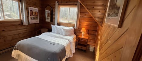 A log cabin bedroom with a bed, bedside tables, and framed pictures on the walls.