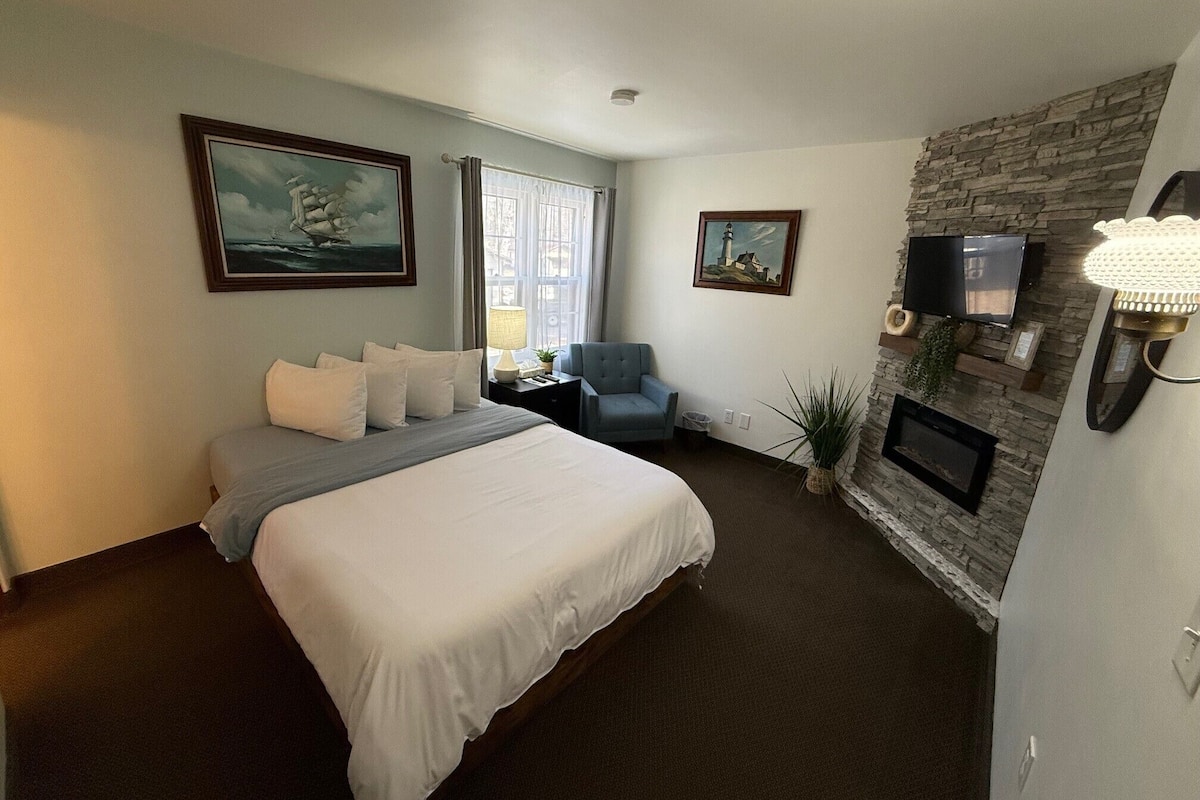 A hotel room with a bed, a chair, a TV, a fireplace, and artwork on the walls.