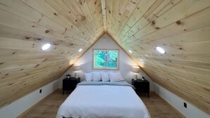 A bedroom with a sloped ceiling, a bed, two bedside tables, and a window. - Scott's Superior Inn and Cabins (Ontonagon)