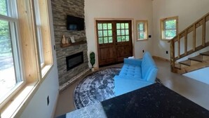 A spacious living room with a stone fireplace, a blue sofa, and a wooden staircase. - Scott's Superior Inn and Cabins (Ontonagon)