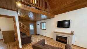 A spacious living room with a fireplace, a television, and a staircase leading to an upper level. - Scott's Superior Inn and Cabins (Ontonagon)