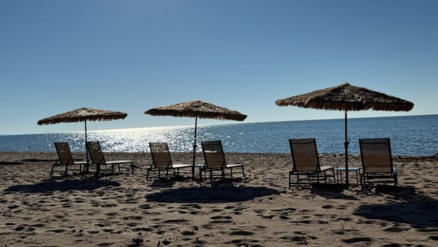 A beach with four sun umbrellas and six lounge chairs facing the ocean. - Scott's Superior Inn and Cabins (Ontonagon)