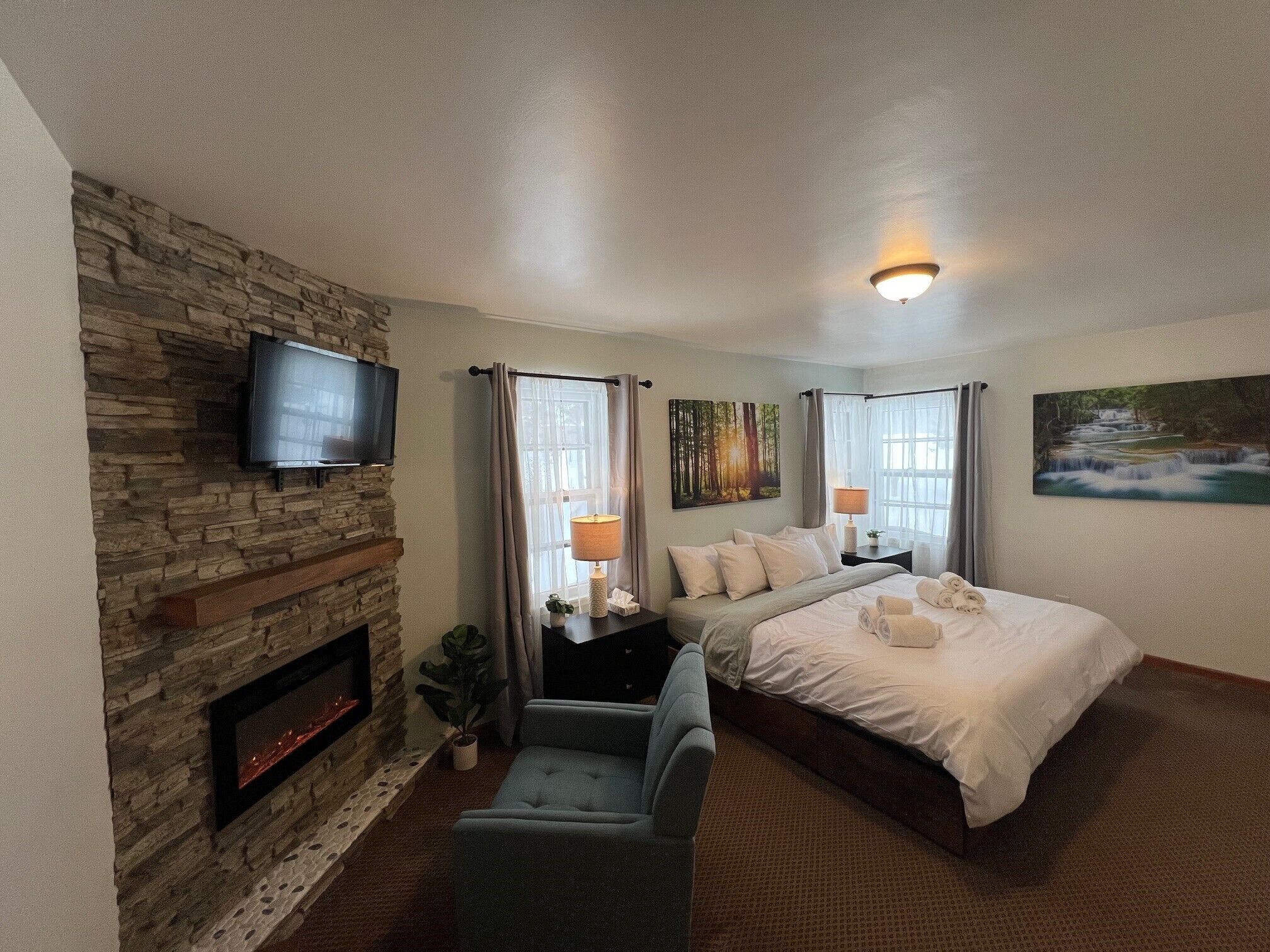A hotel room with a stone fireplace, a bed, a TV, and a painting of a waterfall.