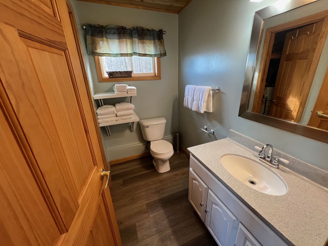 A bathroom with a wooden door, a toilet, a sink, and a mirror.