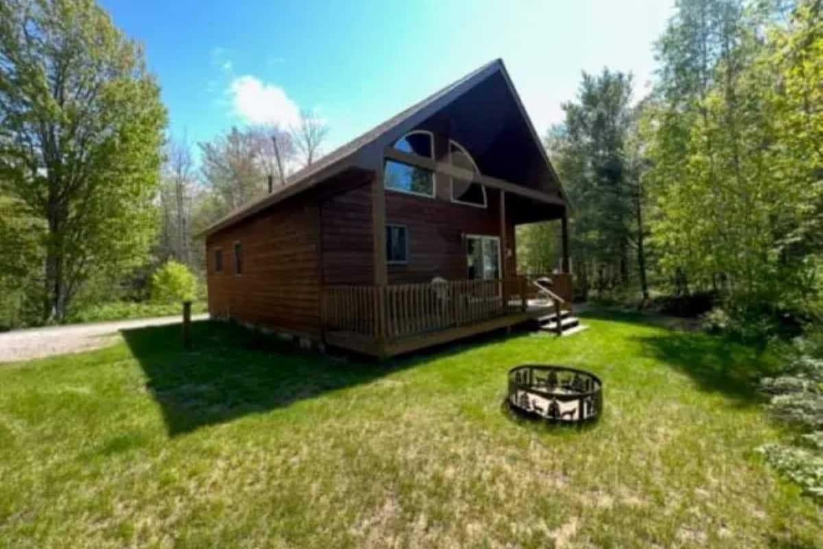 A wooden cabin with a porch, surrounded by a grassy yard and trees.
