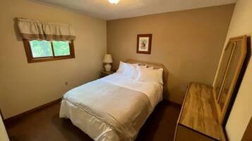 A bedroom with a bed, a nightstand, a dresser, a window with curtains, and a ceiling light.