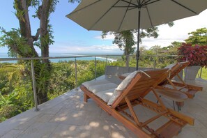 Eine Terrasse mit zwei Holzliegen, einem Sonnenschirm und Blick auf das Meer.