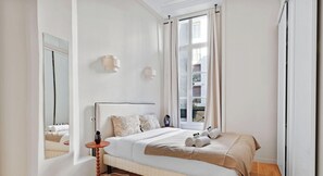 Ein Schlafzimmer mit Bett, Nachttisch, Spiegel und einem Fenster mit Vorhängen.