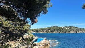 Eine Küstenlandschaft mit klarem, blauem Wasser, felsigem Gelände und einem kleinen Gebäude mit Pool.