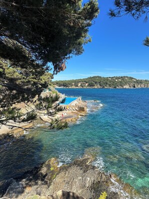 Eine Küstenlandschaft mit klarem, blauem Wasser, felsigem Gelände und einem kleinen Gebäude mit Pool.