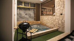 Ein Wellnessbereich mit Whirlpool, Grill und einer Steinwand.