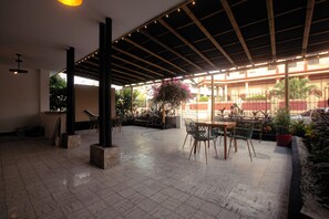 Ein überdachter Innenhofbereich mit gefliestem Boden, einer Holzpergola und Sitzgelegenheiten.