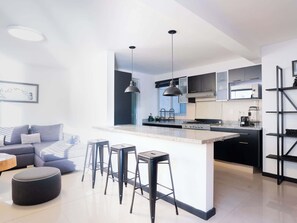 Eine moderne Küche mit Kochinsel, Barhocker und Essbereich mit Sofa und Hocker.