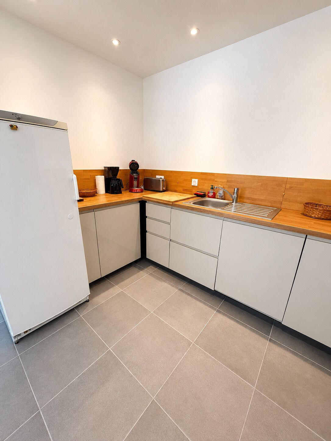 A modern kitchen with a refrigerator, toaster, coffee maker, and sink.