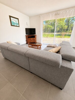 Ein modernes Wohnzimmer mit einem grauen Ecksofa, einem Fernsehschrank aus Holz und einem Glastisch.