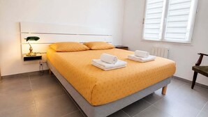 Una cama bien tendida con un edredón amarillo, una lámpara de noche y una lámpara colgante roja.