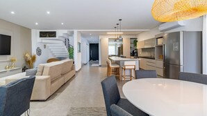 Una cocina moderna con una isla central, un comedor con una mesa redonda y una sala de estar con sofá y sillones.