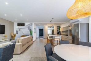 Eine moderne Küche mit einer zentralen Kochinsel, ein Essbereich mit rundem Tisch und ein Wohnzimmer mit Sofa und Sesseln.