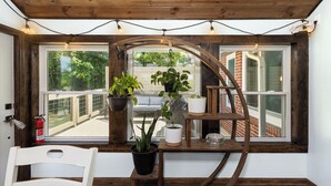 A room with a wooden bench, a white chair, and a window with a view of a brick building and greenery.