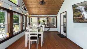 A dining area with a wooden ceiling, large windows, and a view of the outdoors.