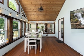A dining area with a wooden ceiling, large windows, and a view of the outdoors.