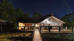 A house with a covered patio, a wooden deck, and a fenced yard at night.