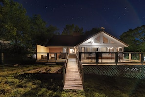 A house with a covered patio, a wooden deck, and a fenced yard at night.