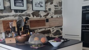Eine Küche mit einer Steinwand, weißen Schränken und einer großen Kochinsel mit verschiedenen Küchenutensilien und einer Obstschale.