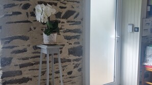 Ein Zimmer mit Steinwand, einer weißen Tür, Fliesenboden und einem kleinen weißen Tisch mit einer Pflanze.