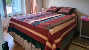 Ein Schlafzimmer mit einem großen Bett, einem Fenster mit Vorhängen, einem Heizkörper und einem Holzboden.