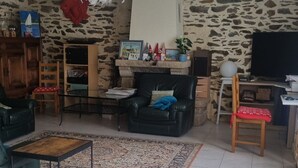 Ein Wohnzimmer mit einer Steinswand, einer schwarzen Ledersofa, einem Holzstuhl, einem kleinen Tisch und einem Fernseher.
