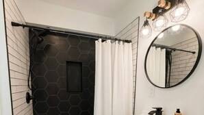 Een badkamer met een douche, een witte wastafel, een spiegel en een zwart, honingraatpatroon op de wand.