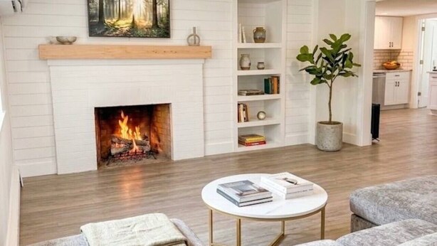 Een woonkamer met een open haard, een bank, een bijzettafeltje en een boekenplank.