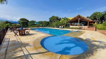 Una piscina con solárium, sillas de descanso y un área de estar cubierta.