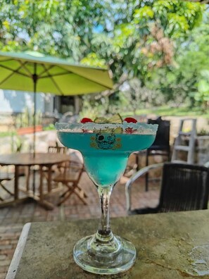 A cocktail in a glass with a decorative rim, placed on an outdoor table with chairs and an umbrella in the background. - Suite between mountains I Jacuzzi and turkish bath at Hotel Toscana (Tena)