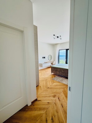 Ein modernes Interieur mit einem Fischgrätparkett, einem Bett, einem Schreibtisch und einem großen Fenster mit Blick.