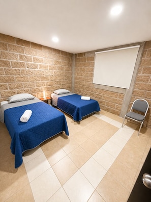 A room with two beds, a projector screen, a chair, and a tiled floor.
